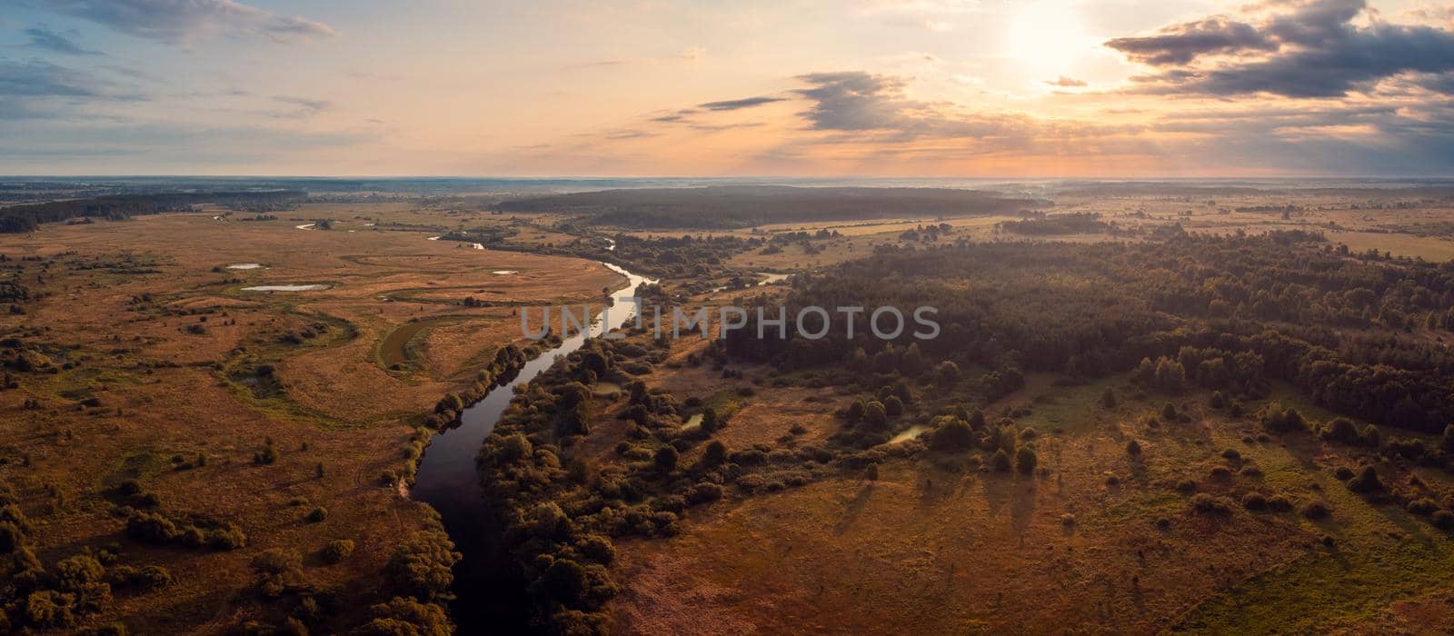 Wide panorama of small river in the countryside in the morning with rising sun on the background