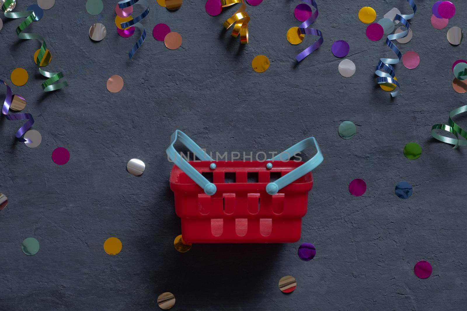 Shopping basket and festive tinsel flat lay on dark background. Top view.