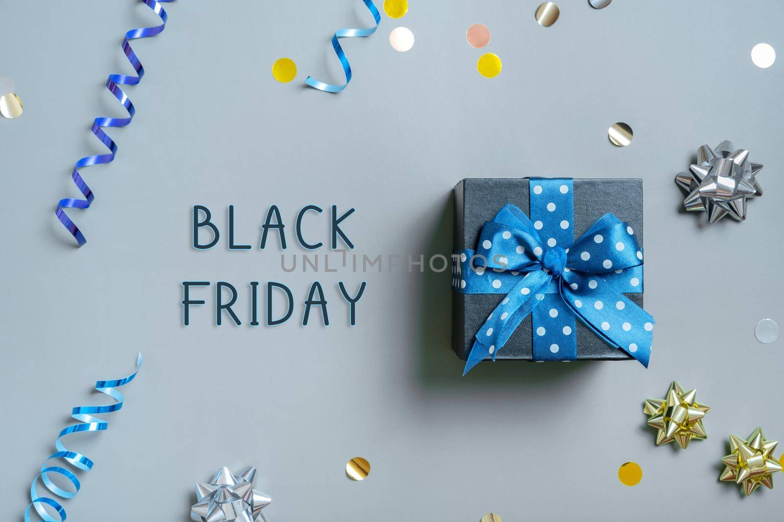 Black Friday text with gift box and festive tinsel flat lay on grey background. Top view.
