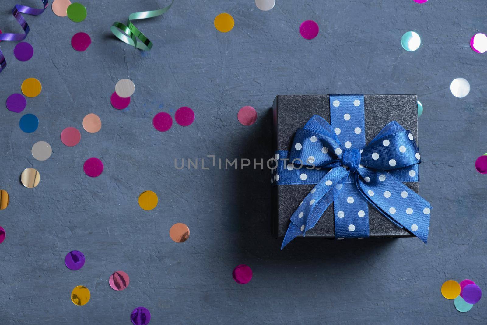 Black gift box with bow and holiday tinsel flat lay on dark cement background. Top view by ssvimaliss