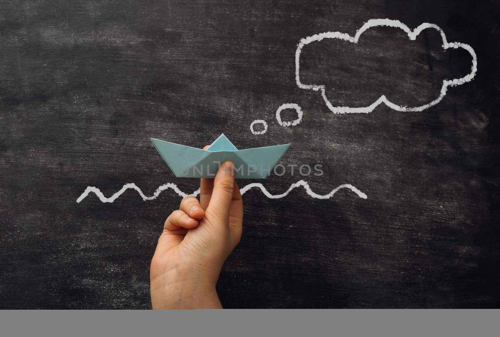Woman holds paper ship near chalkboard with drawn thinking bubble and waves closeup. Sailing right direction. Business development