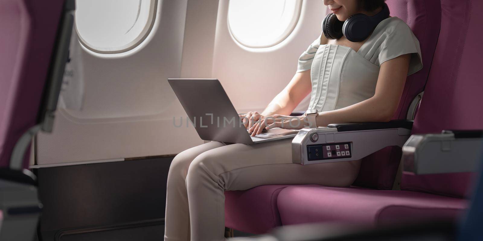 Joyful asian woman sits in the airplane and using mobile phone while go to travel.