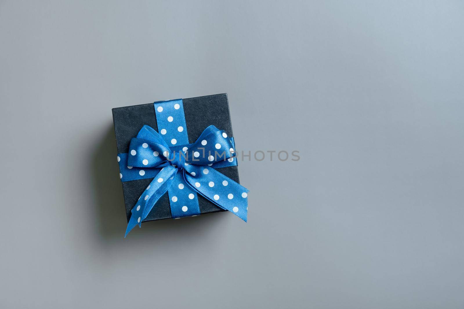 Black gift box with bow flat lay on grey background. View from above. Copy space.