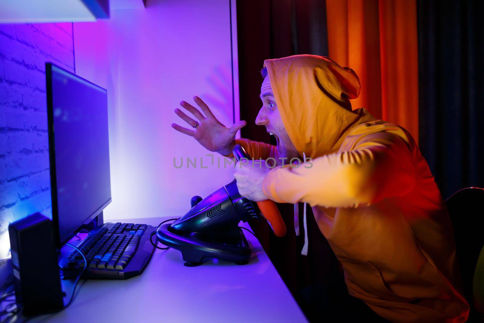 Male gamer playing racing games on the computer. He uses the steering wheel. Emotional game
