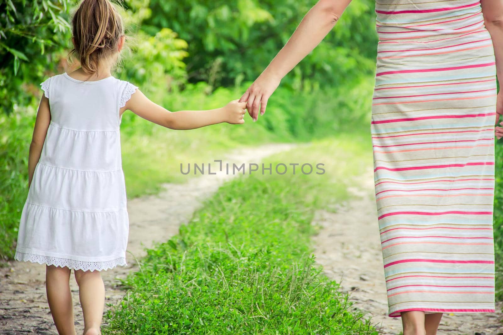 Mom and daughter are walking along the road holding hands.
