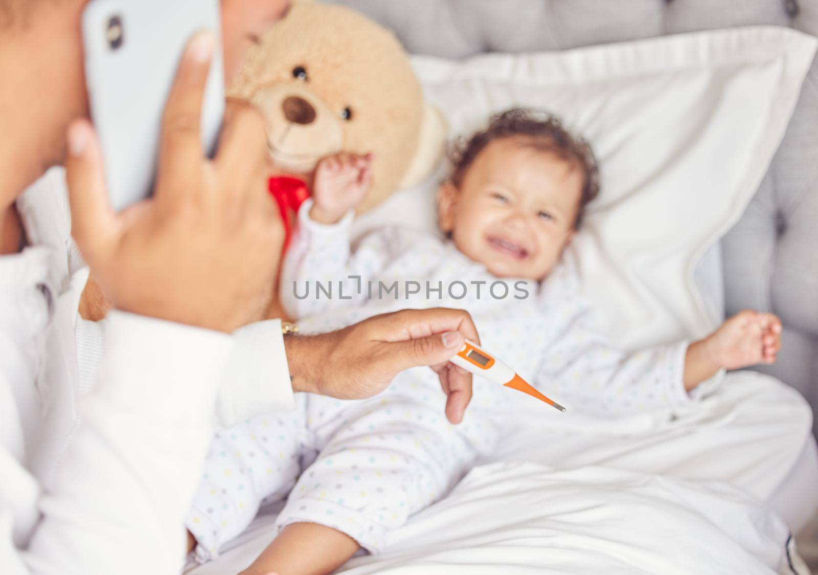 Sick child with covid or flu, mother with thermometer in hand and calling doctor for crying child. Kid with bad fever, may go to hospital or clinic and get emergency medical help to save babies life by YuriArcurs