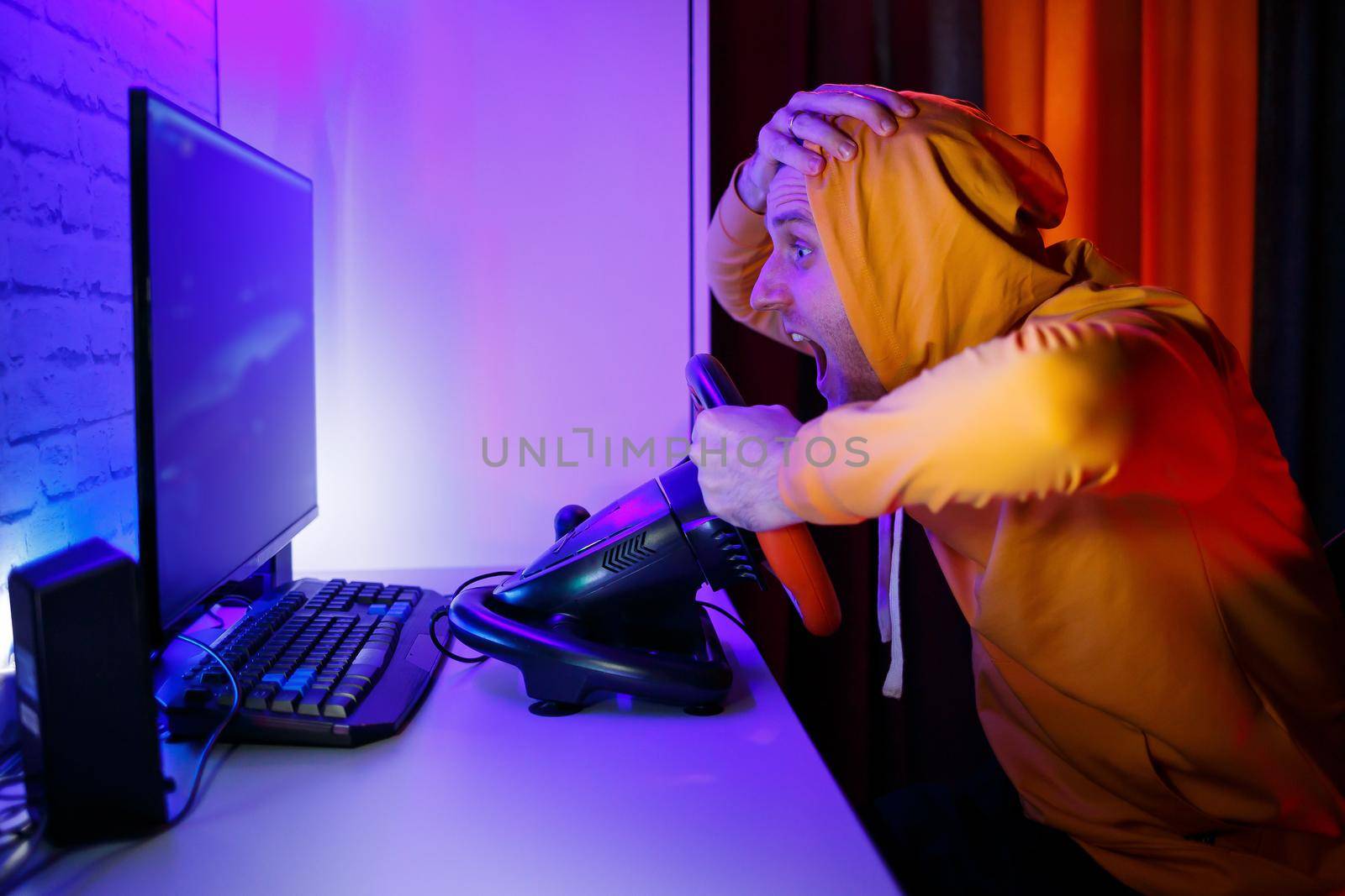 Male gamer playing racing games on the computer. He uses the steering wheel. Emotional game