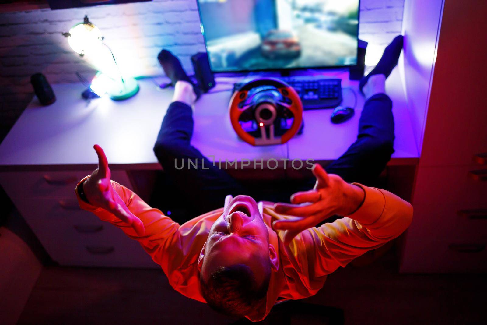Male gamer playing racing games on the computer. He uses the steering wheel. Emotional game