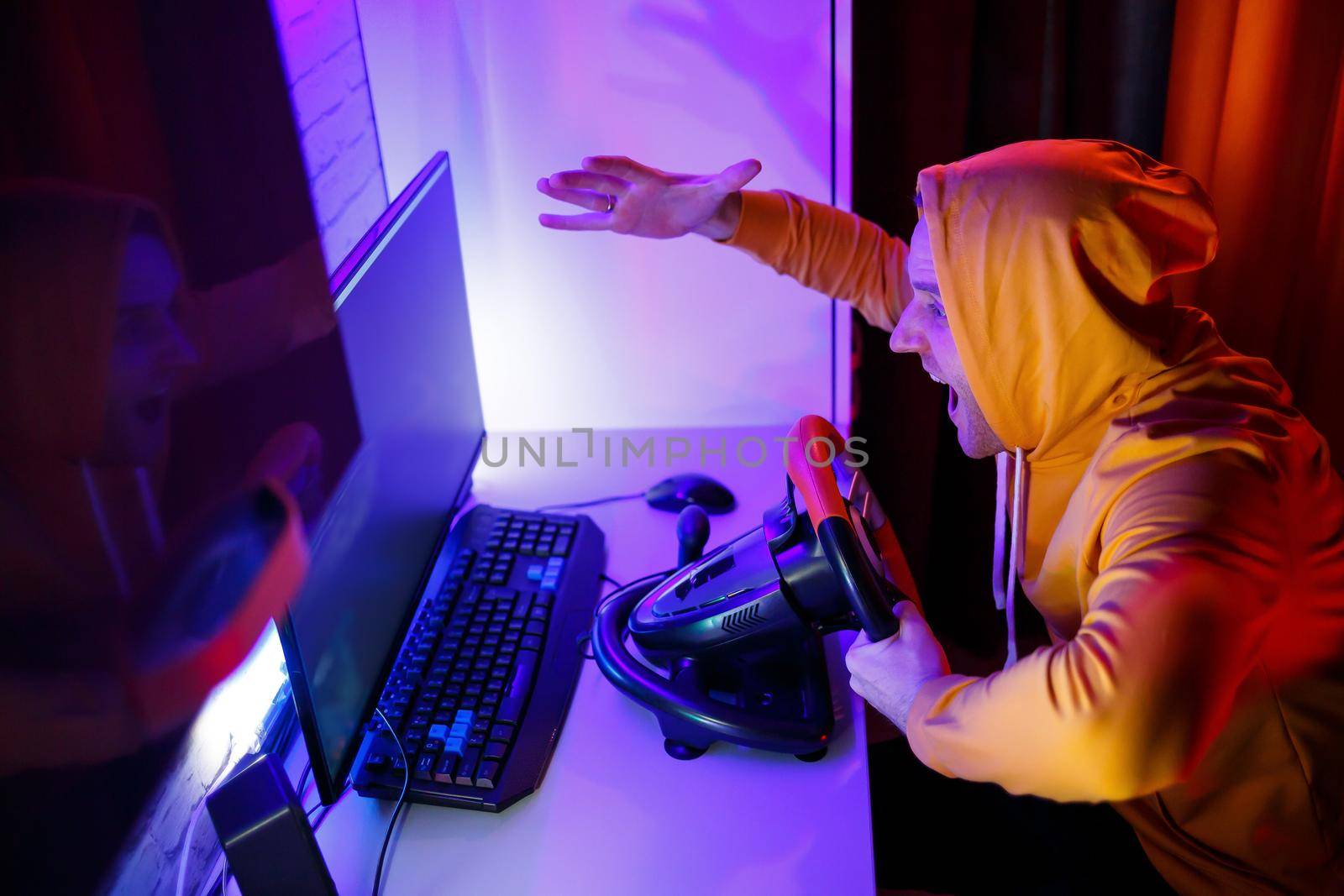 Male gamer playing racing games on the computer. He uses the steering wheel. Emotional game