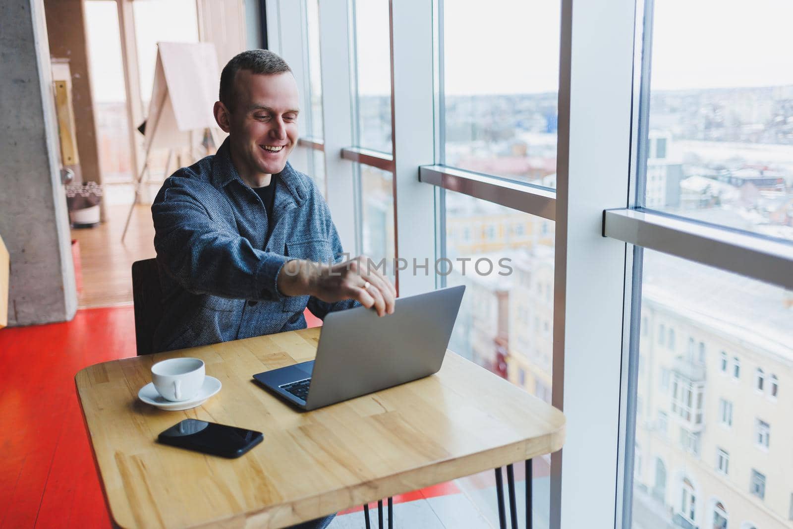 Successful happy business man is sitting at a table in a cafe, holding a cup of coffee and using a laptop.