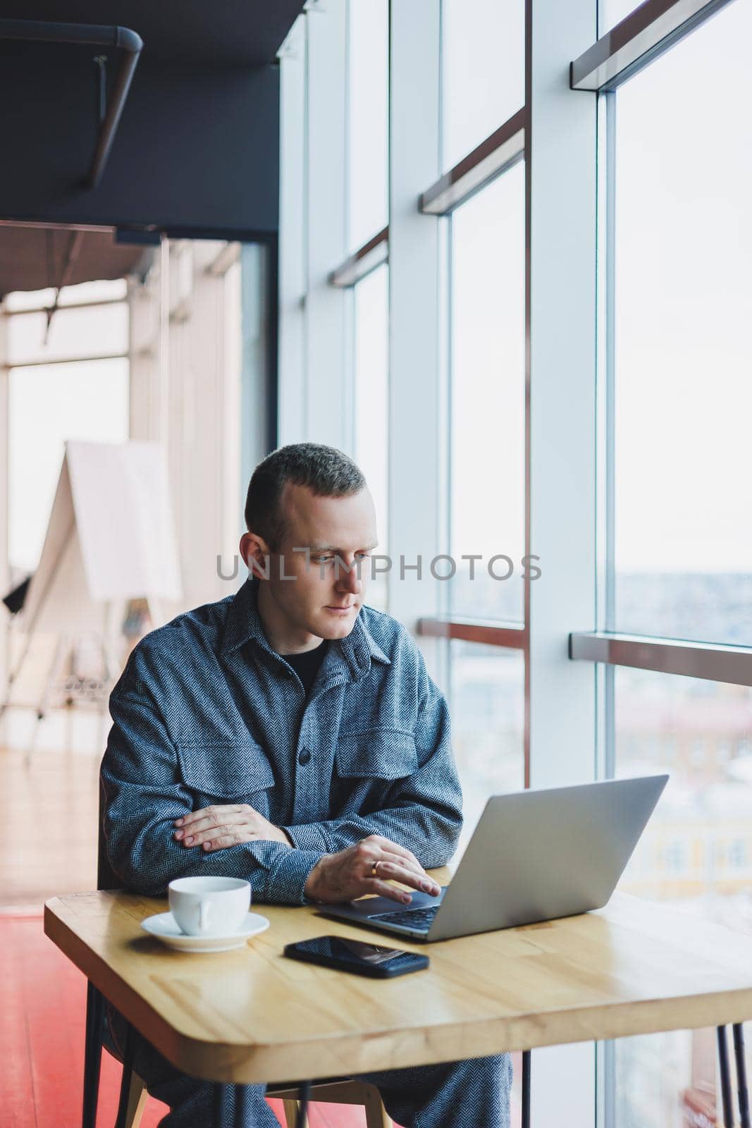 Successful happy business man is sitting at a table in a cafe, holding a cup of coffee and using a laptop. by Dmitrytph