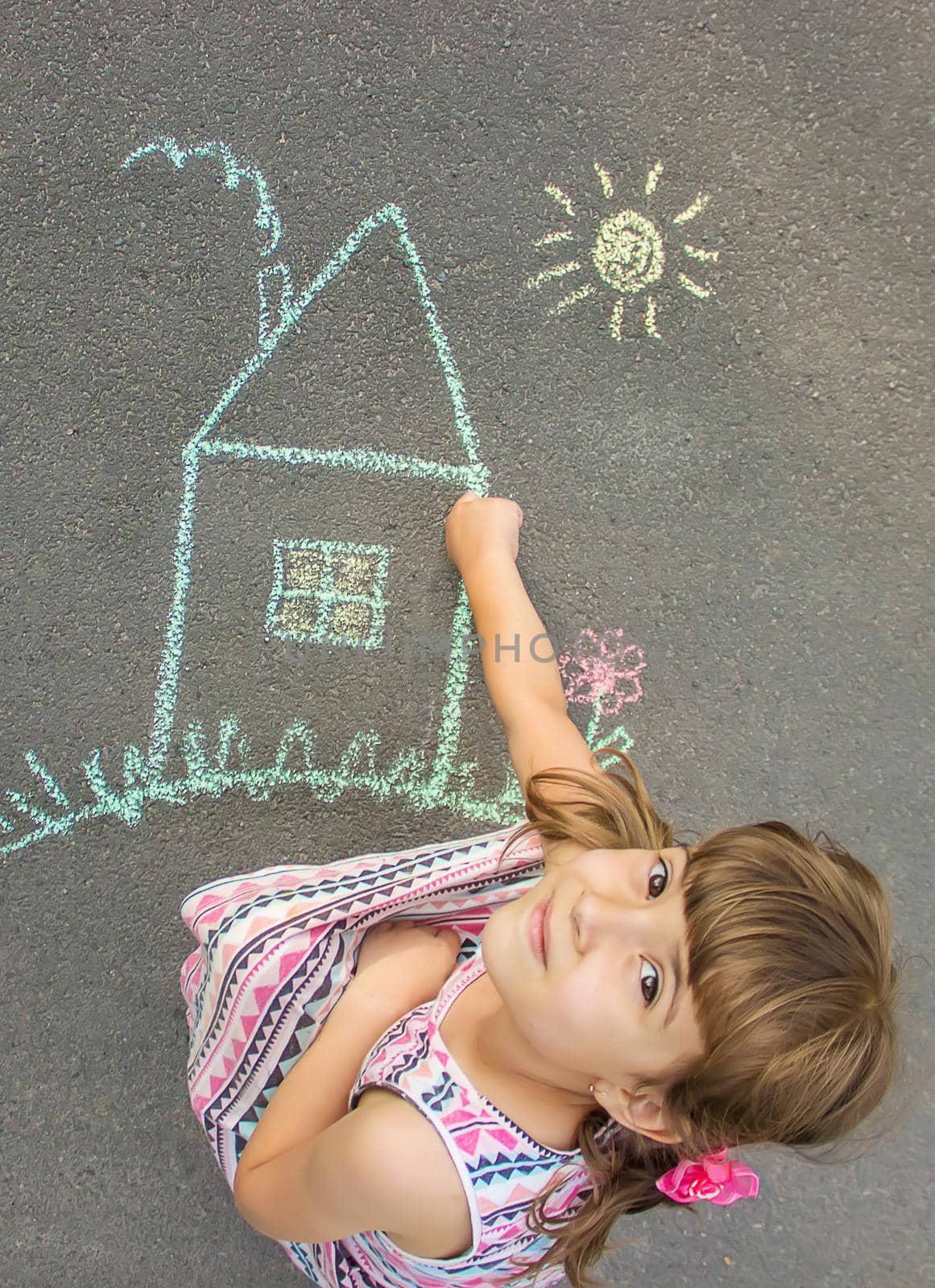 The child draws the house with chalk on the asphalt. Selective focus. by yanadjana
