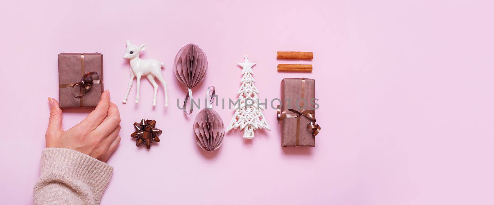 Festive minimal creative christmas composition with gifts, paper balls and female hand flat lay on pink background.
