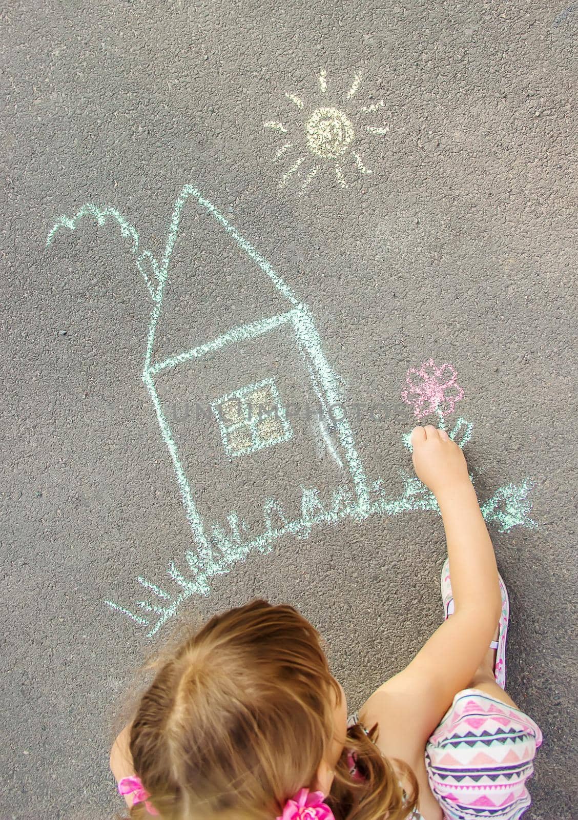 The child draws the house with chalk on the asphalt. Selective focus. by yanadjana