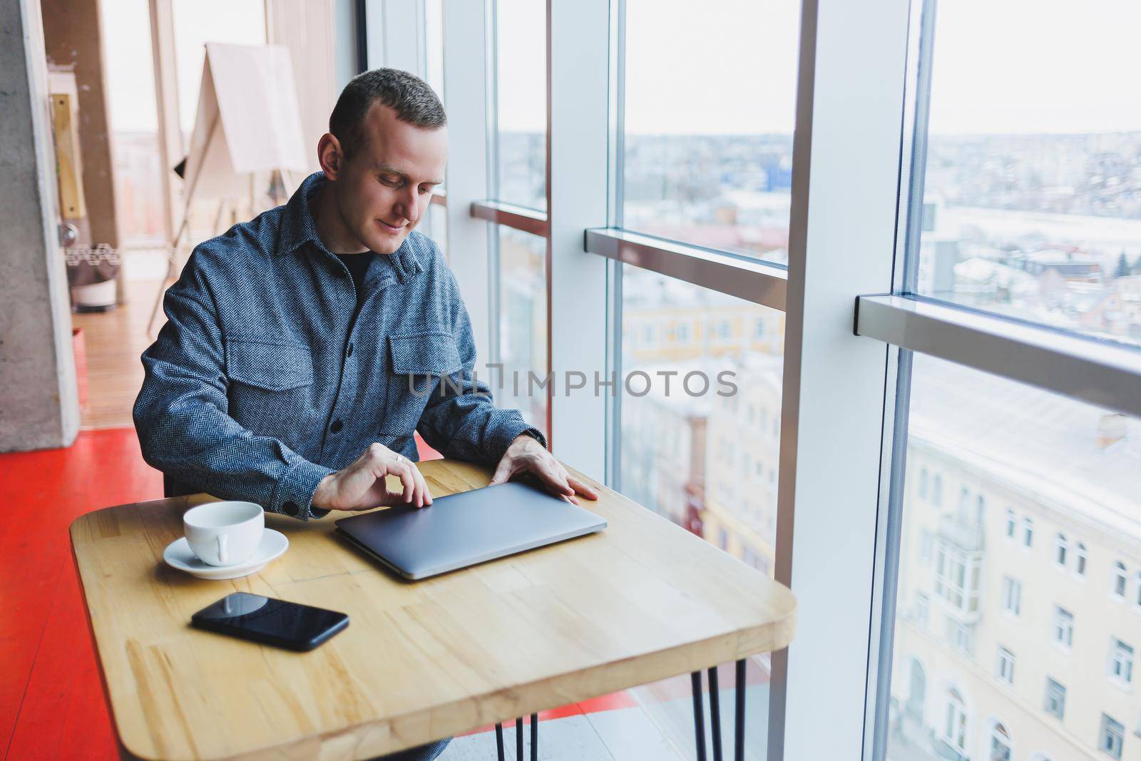 A young successful businessman in a suit drinks coffee and works in a cafe on wireless free internet on a laptop, sitting alone at a table in a cafe.