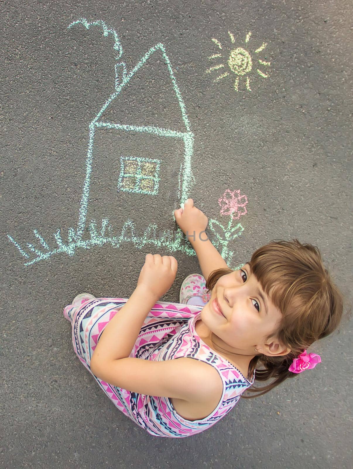 The child draws the house with chalk on the asphalt. Selective focus. by yanadjana