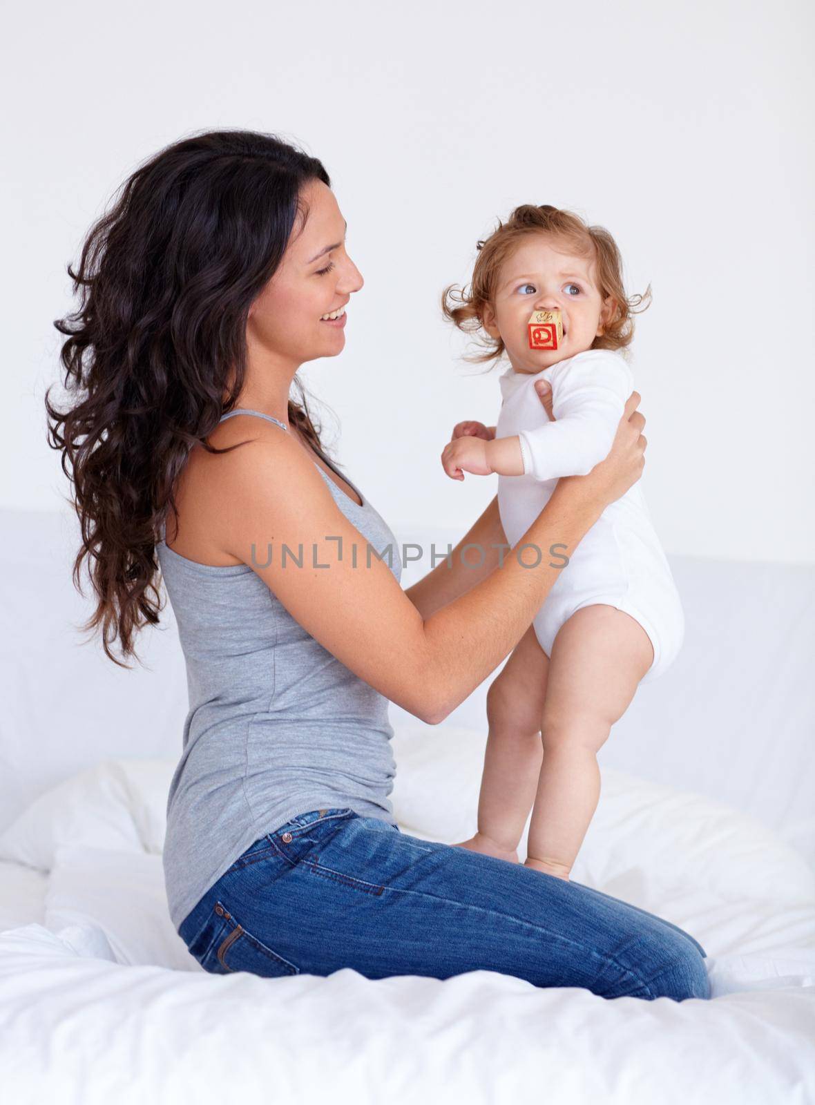 Relaxing at home with my little girl. Image of a mother sitting on her bed and holding up her baby daughter