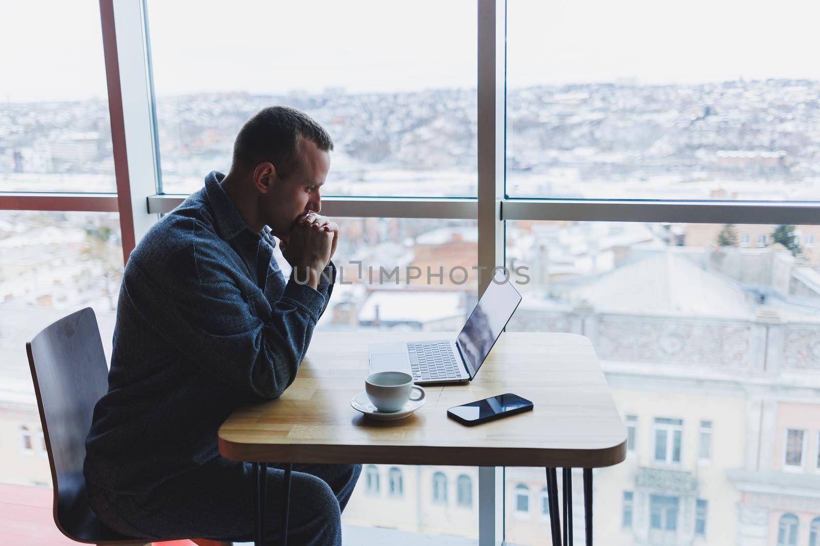 A young successful businessman in a suit drinks coffee and works in a cafe on wireless free internet on a laptop, sitting alone at a table in a cafe.