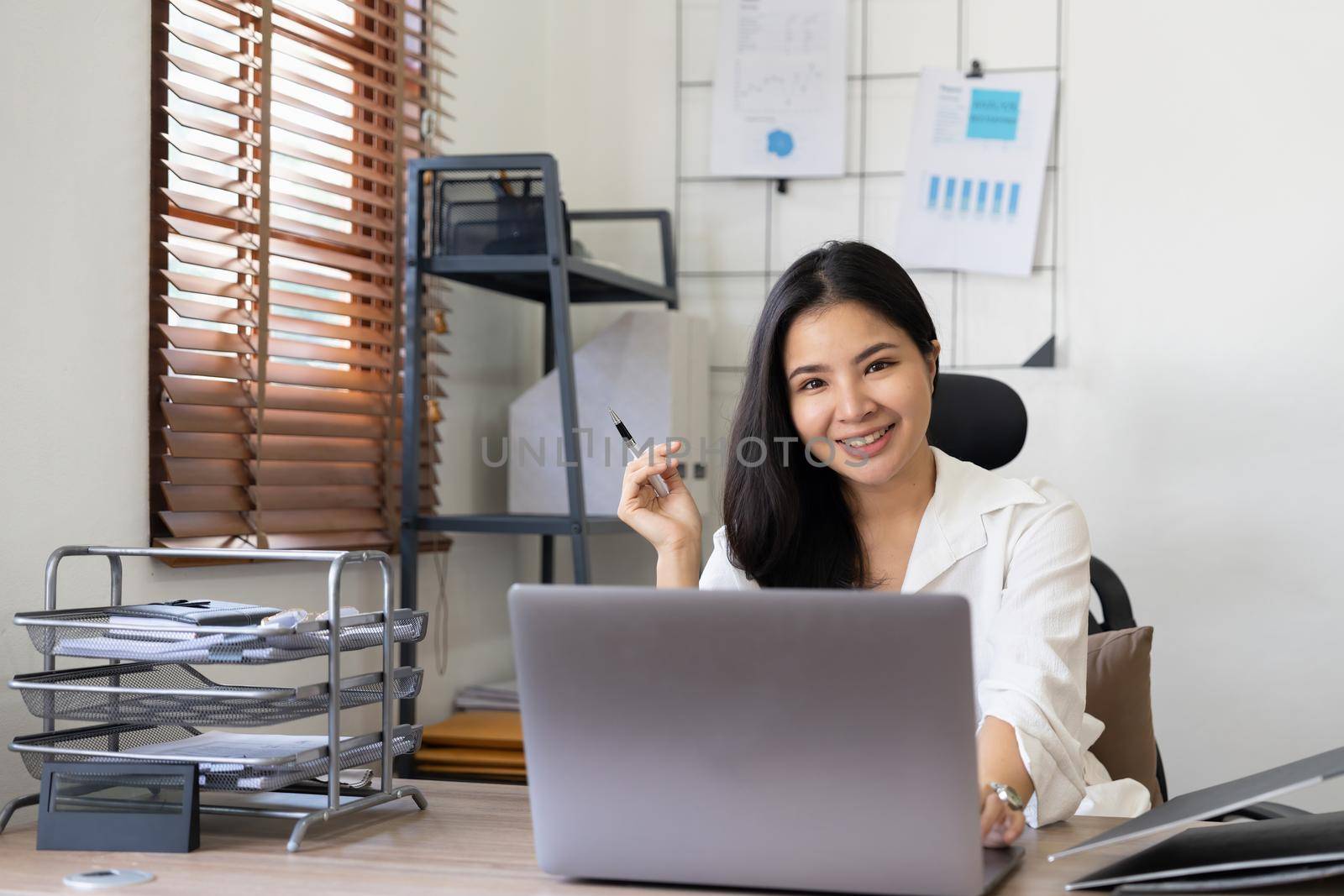 Photo of joyful nice woman using laptop and smiling while sitting at office