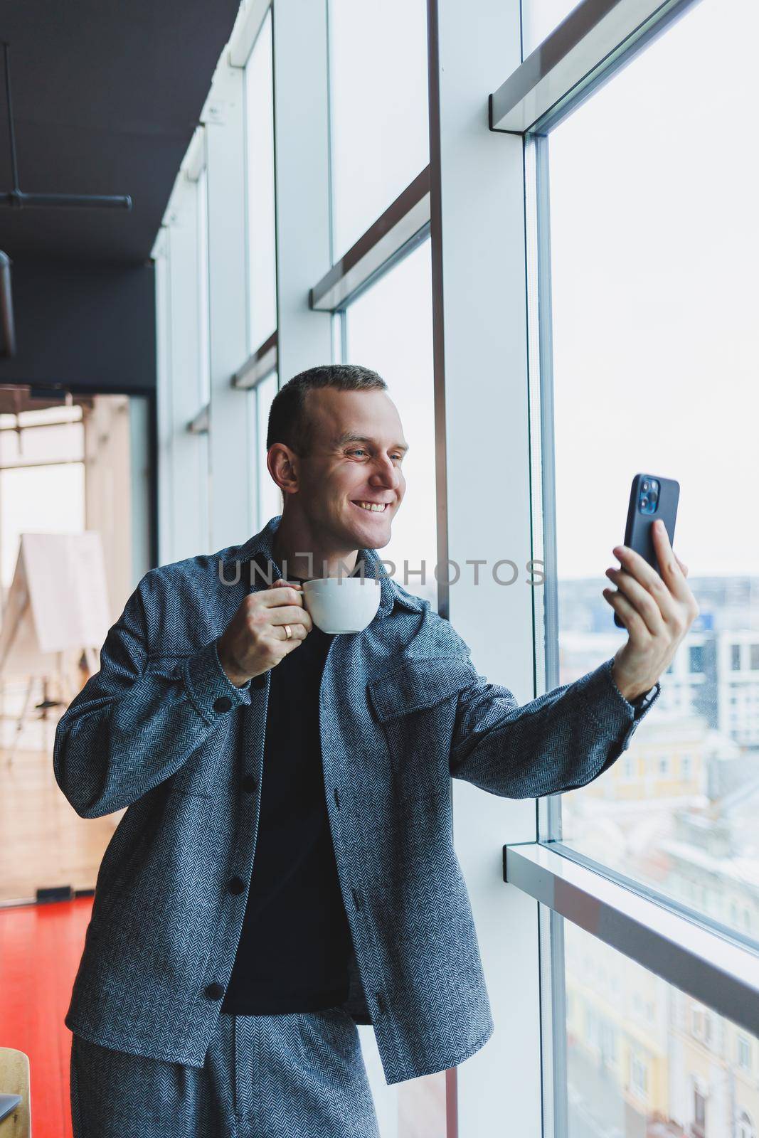 European male freelancer in checking notification on smartphone about money transactions, doing business online, working remotely while in cafe and drinking coffee
