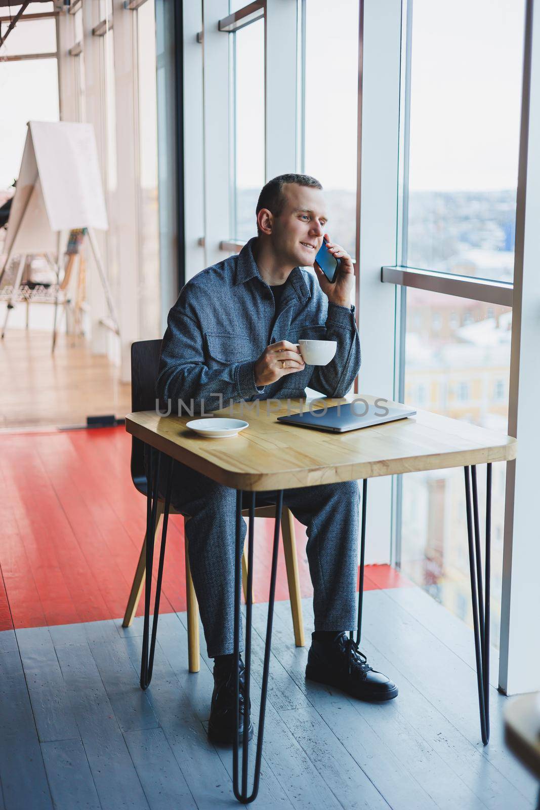 Cheerful IT professional with laptop talking on smartphone to discuss web programming, happy businessman in cafe drinking coffee. freelancer