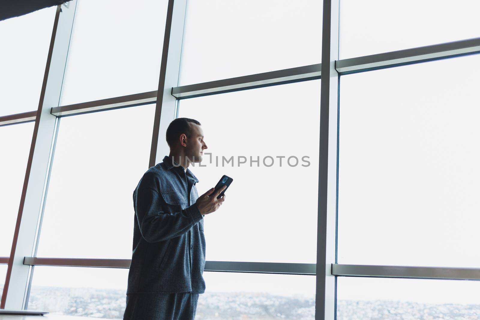 Young business man holding a phone. In an office or business center against the background of large windows of a skyscraper. Work and career, concept