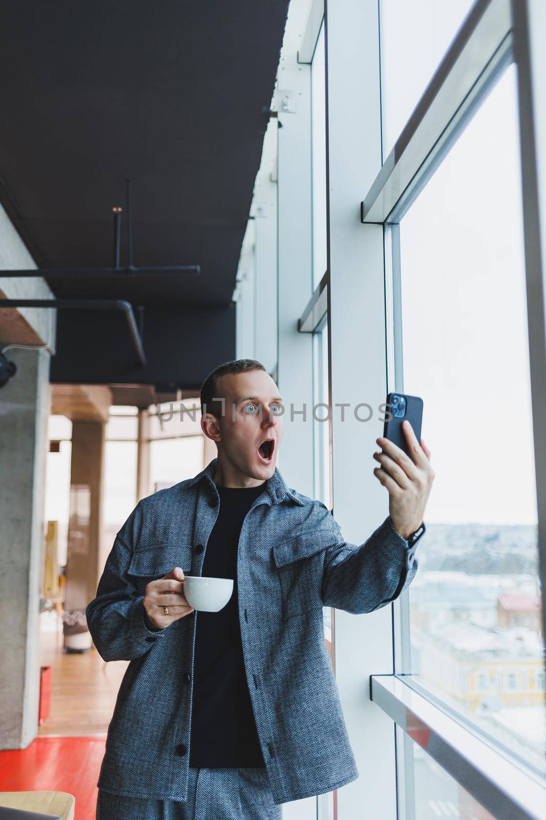 Excited young man in suit using mobile phone with funny expression, excited business man looking at his smartphone, reading good news via email, emotional lifestyle concept.