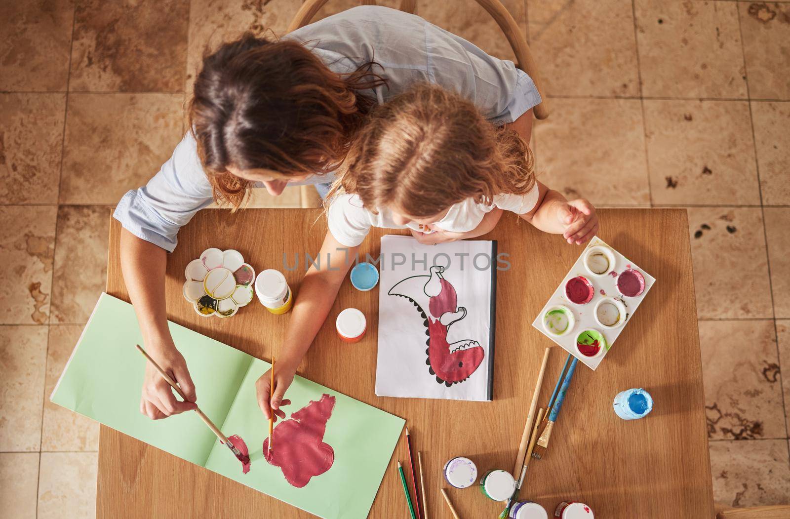 Top view, mother and child art painting in house studio, family home or creative space with brush, oil paint or books. Mom, parent or child hands bonding in abstract design or relax activity on table.
