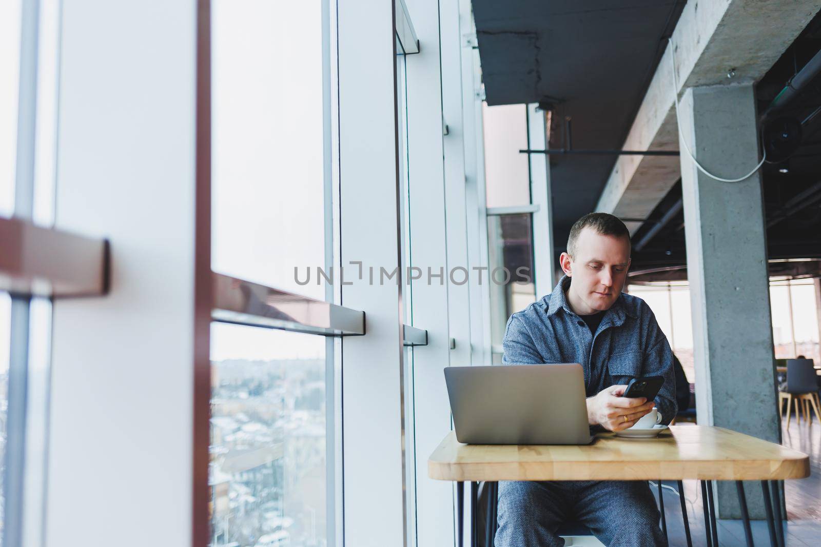 Confident male manager sits at a table in a modern office at a laptop and works, he is talking on the phone, remote work
