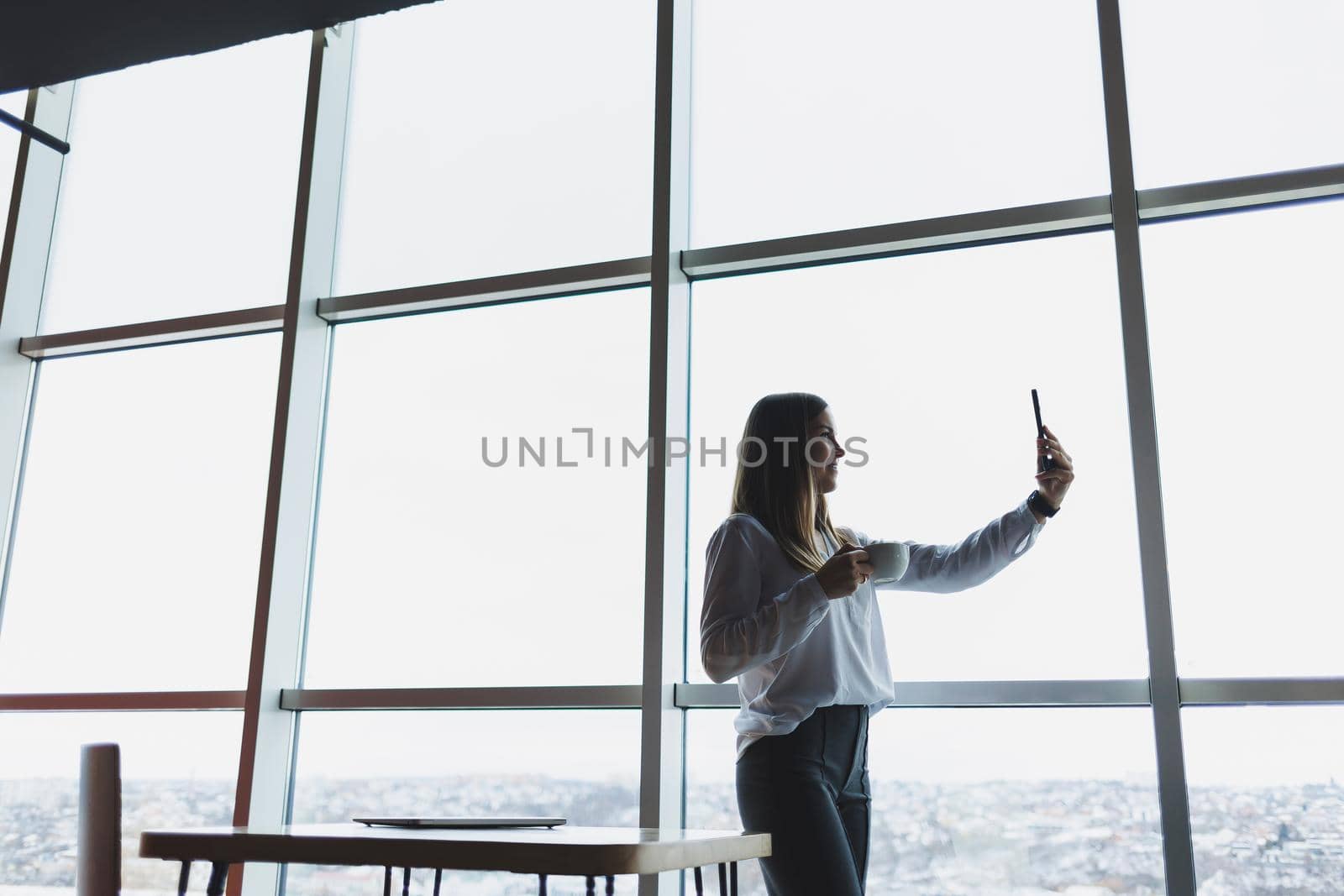 Young businesswoman wearing glasses and holding a phone. In an office or business center against the background of large windows of a skyscraper. Work and career, concept