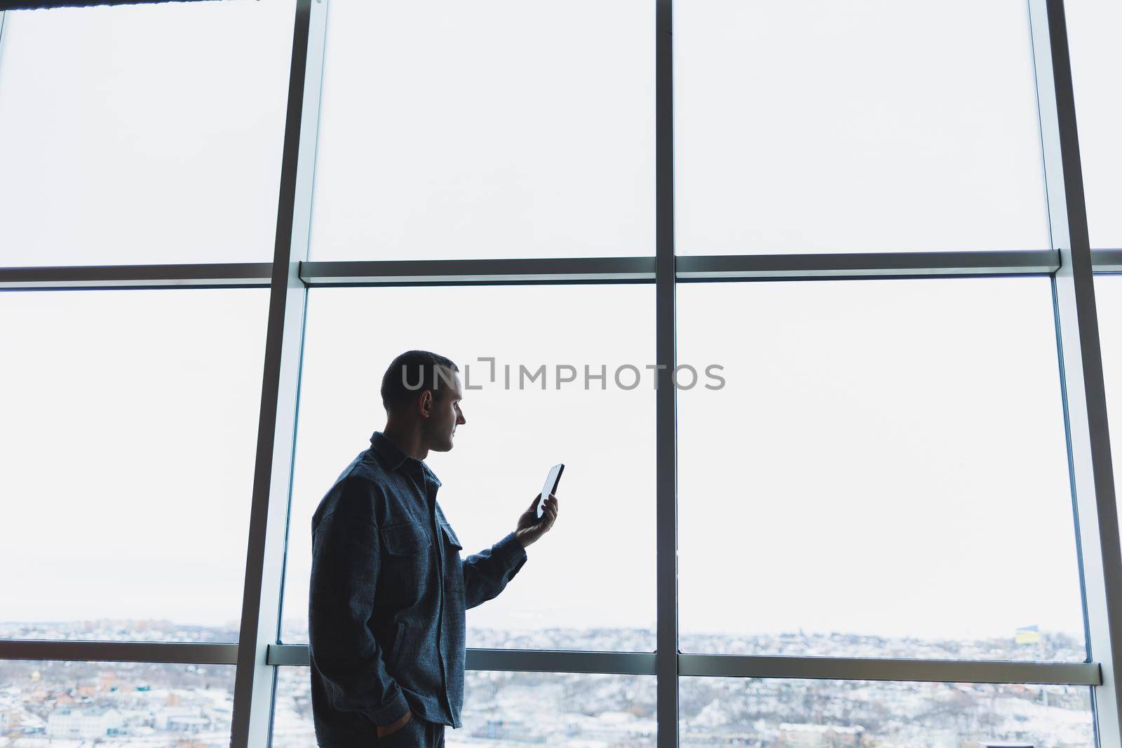 Young business man holding a phone. In an office or business center against the background of large windows of a skyscraper. Work and career, concept