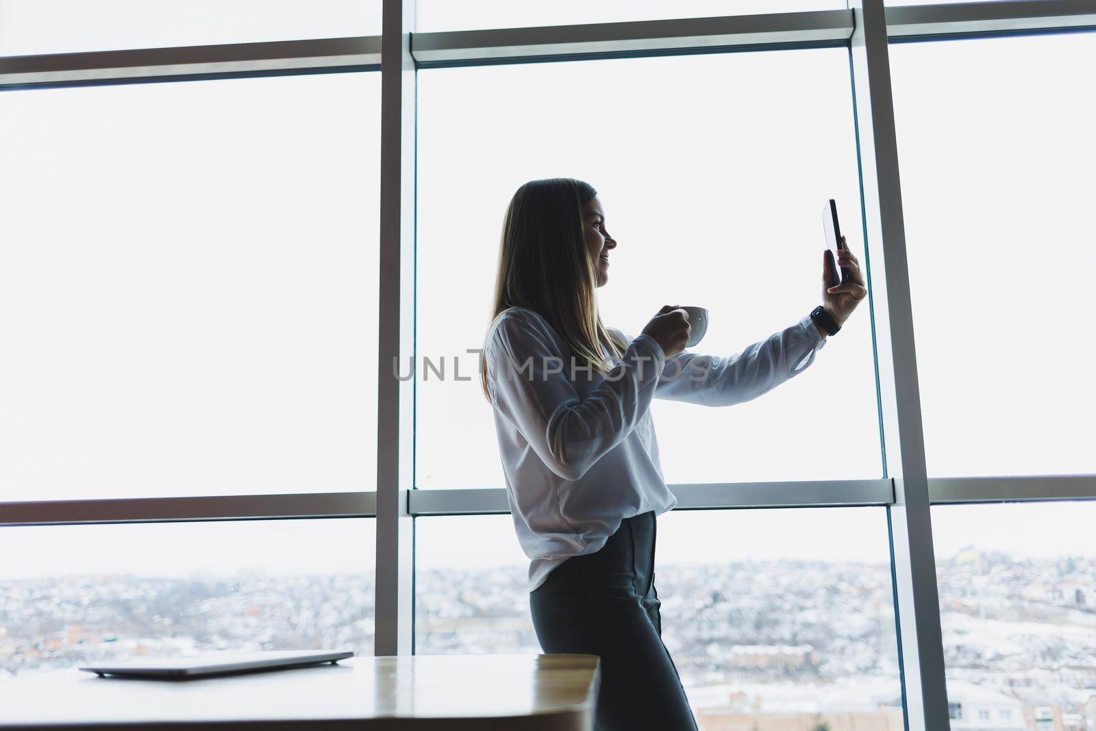 Young businesswoman wearing glasses and holding a phone. In an office or business center against the background of large windows of a skyscraper. Work and career, concept
