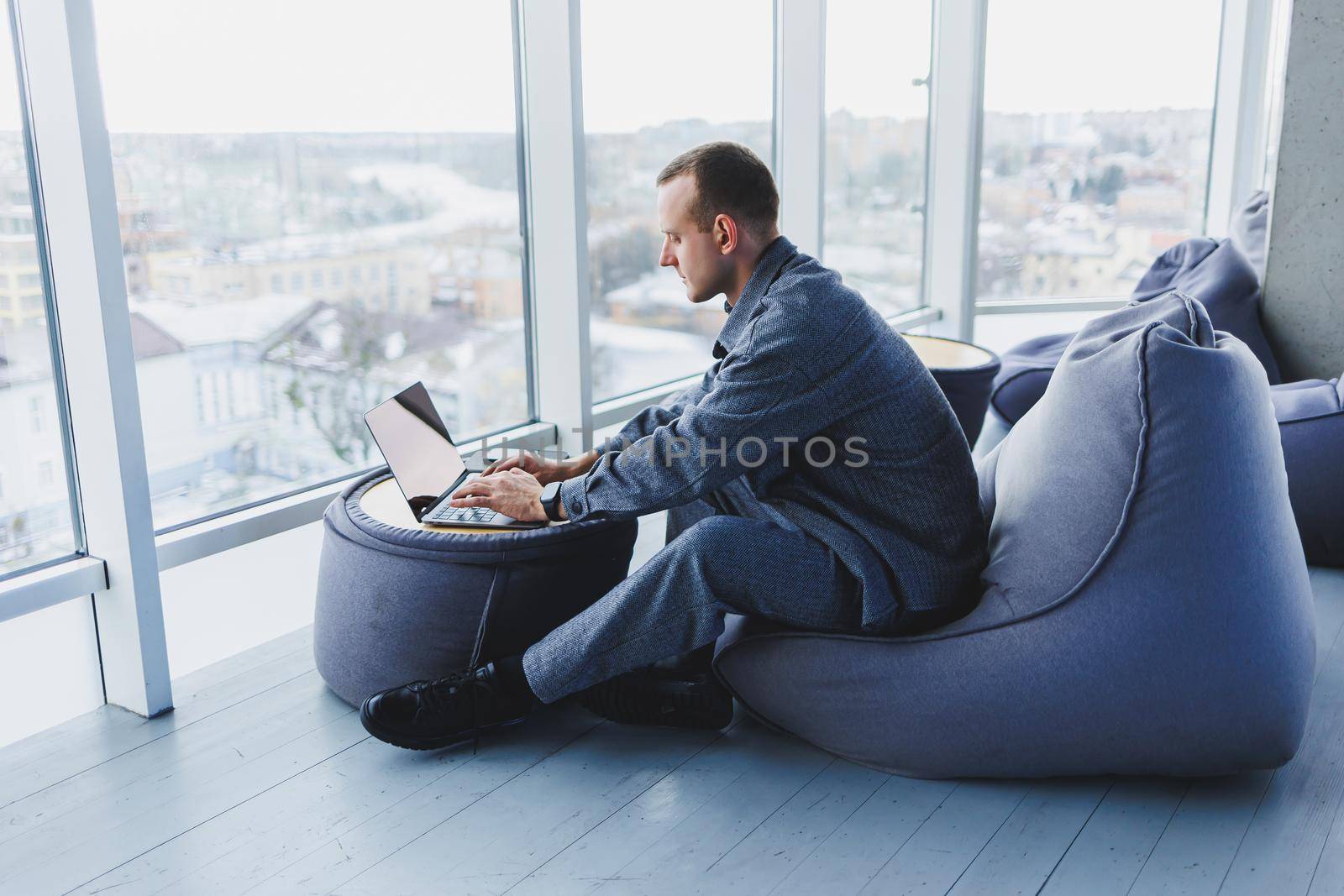 Break. Smiling young man relaxing on bean bag chair while sitting at table and relaxing using laptop, happy businessman leaning back, enjoying work, feeling satisfied