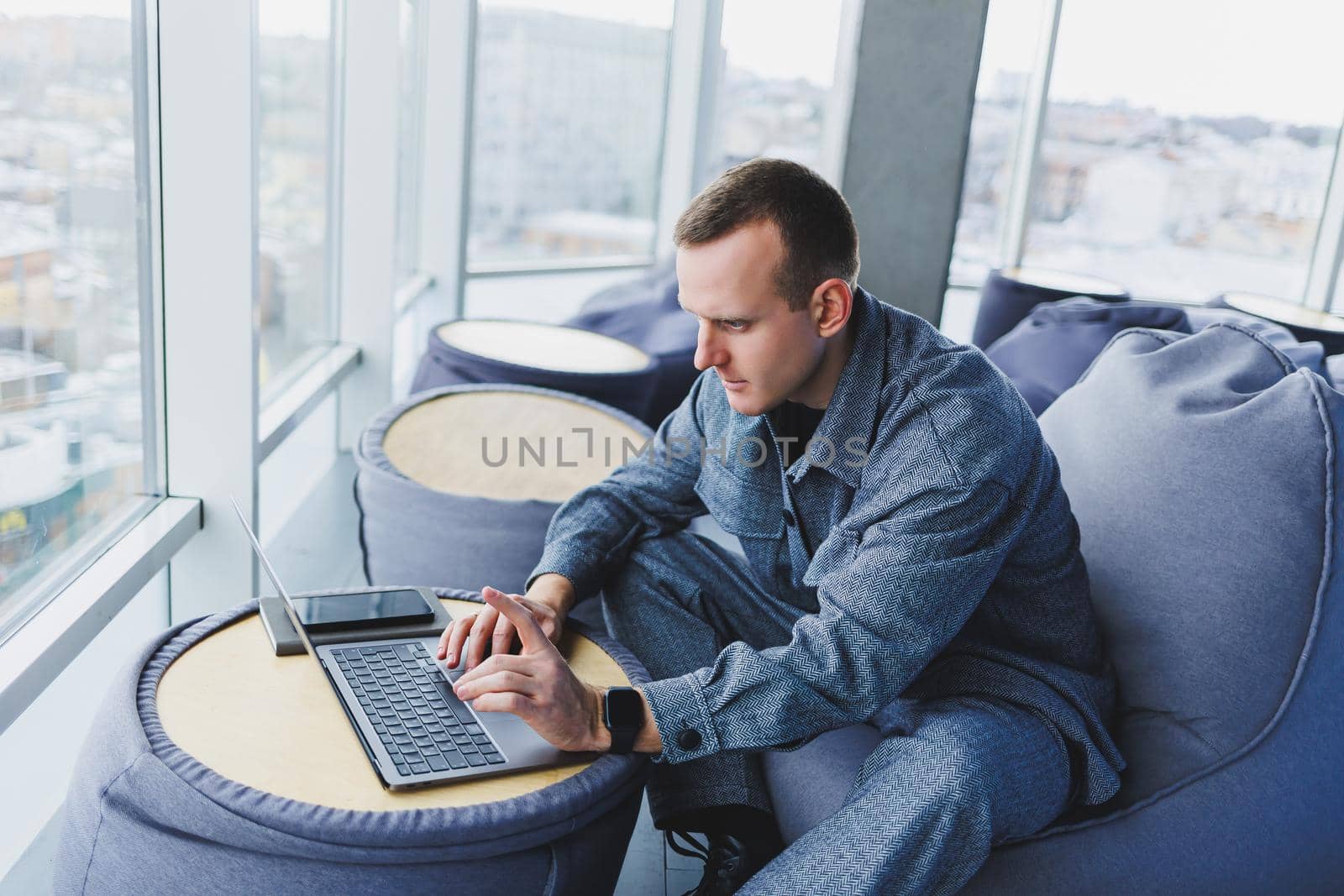 Break. Smiling young man relaxing on bean bag chair while sitting at table and relaxing using laptop, happy businessman leaning back, enjoying work, feeling satisfied