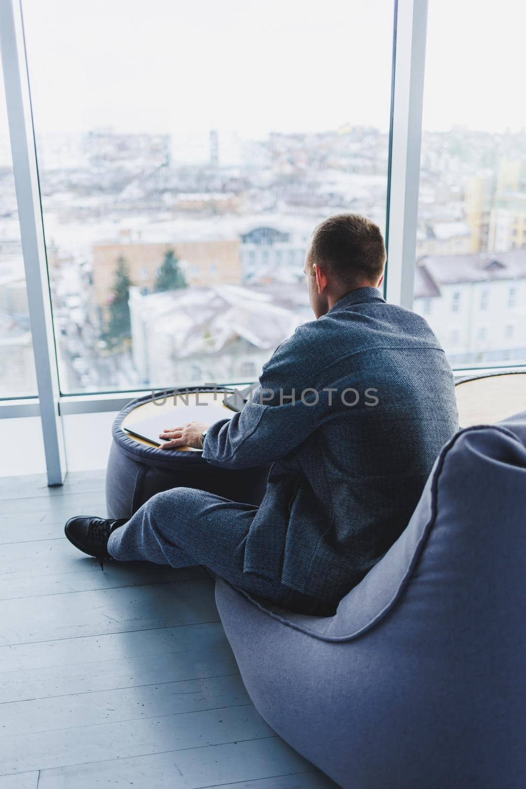 Break. Smiling young man relaxing on bean bag chair while sitting at table and relaxing using laptop, happy businessman leaning back, enjoying work, feeling satisfied