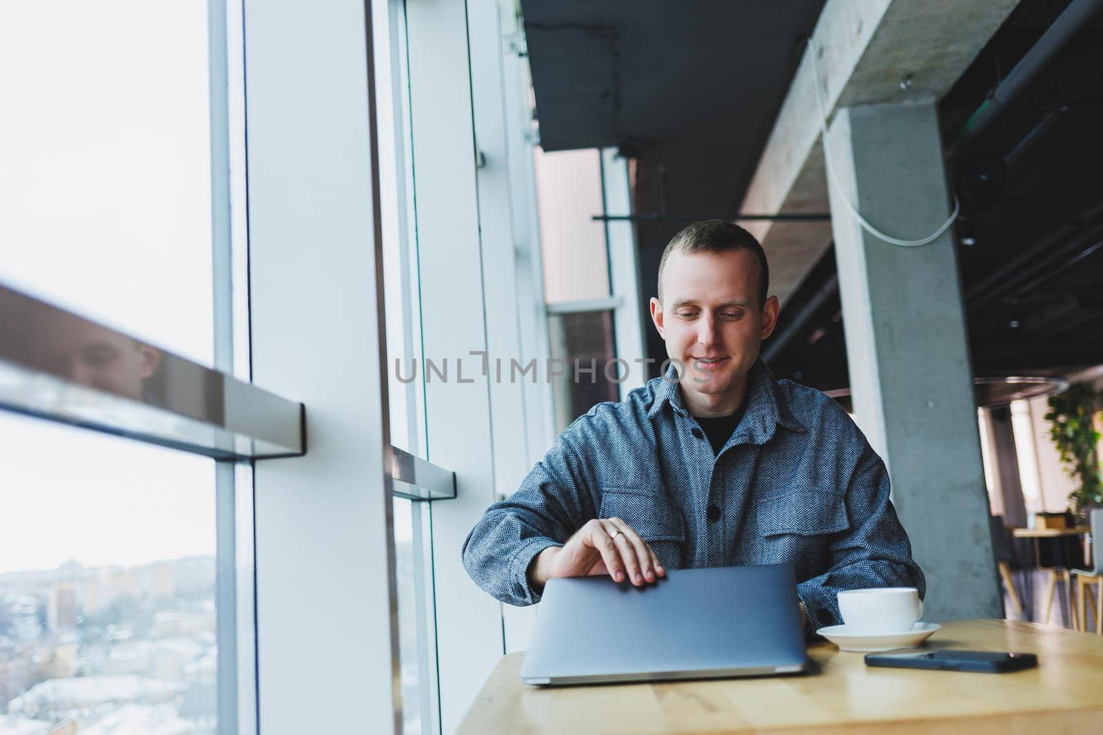 A young successful businessman in a suit drinks coffee and works in a cafe on wireless free internet on a laptop, sitting alone at a table in a cafe.