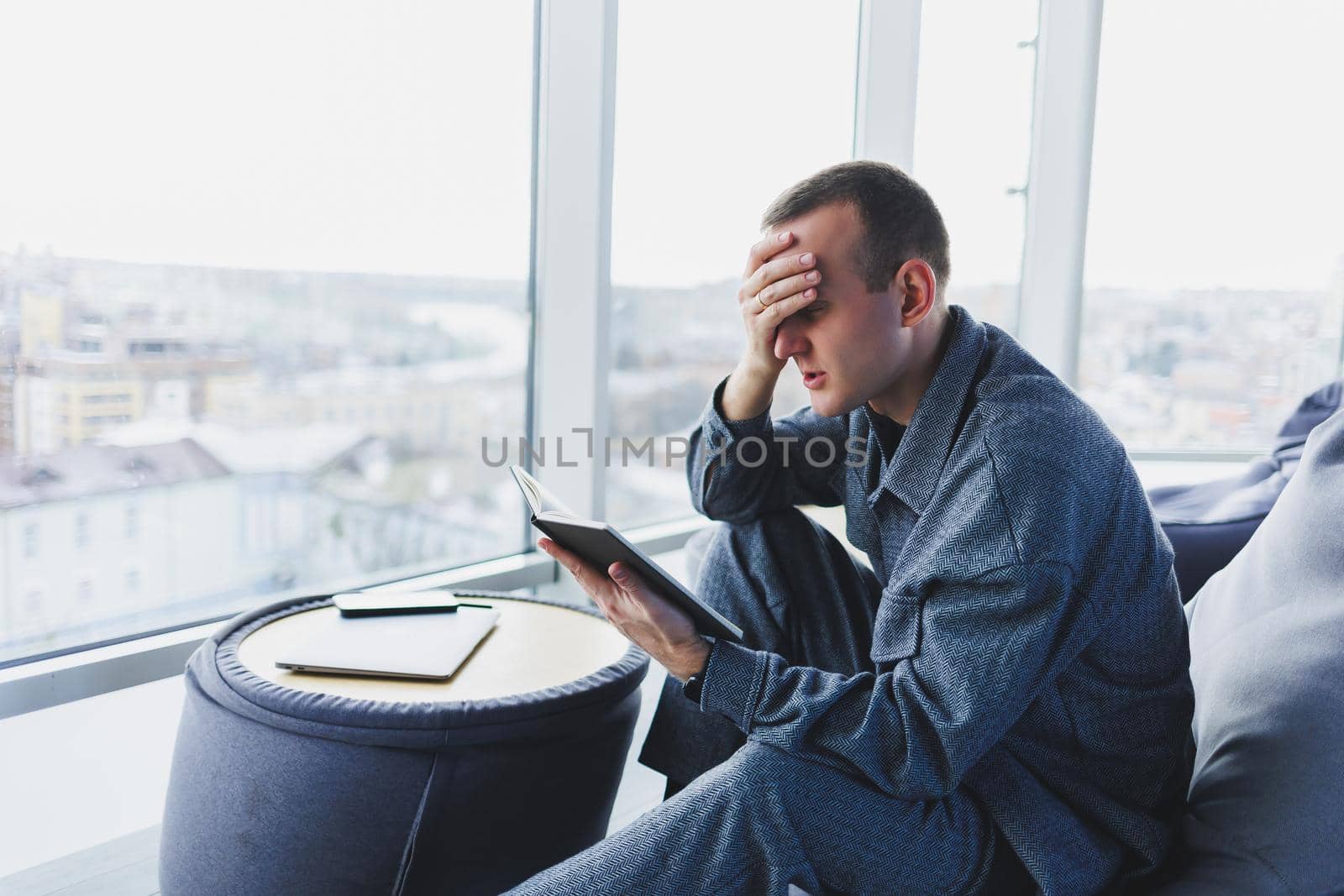 A male businessman in a casual suit resting in a comfortable pouf while working, an attractive freelancer in a suit works remotely and checks notes in a notebook