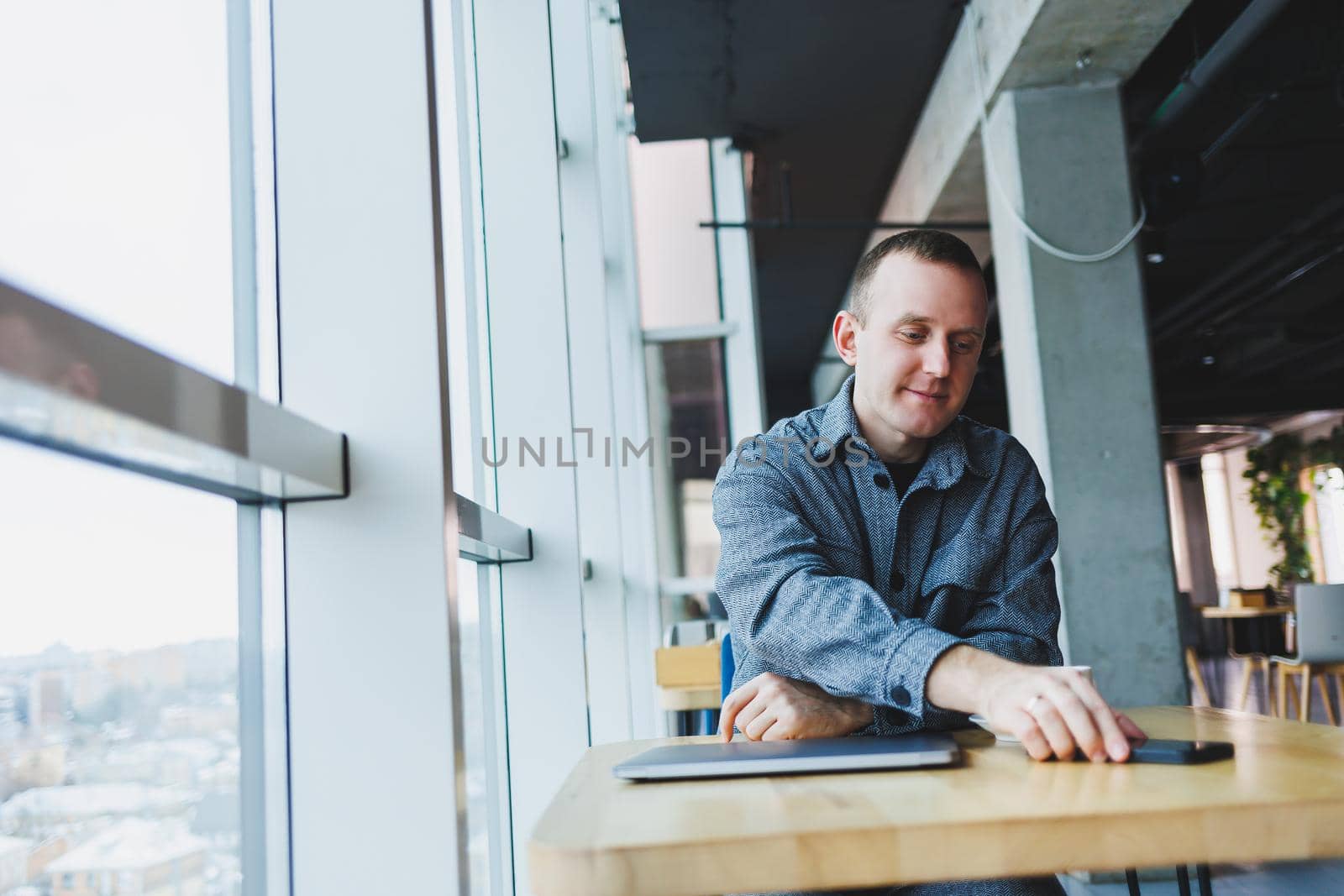 Handsome male manager sits at a table in a modern office with a closed laptop and rests, remote work