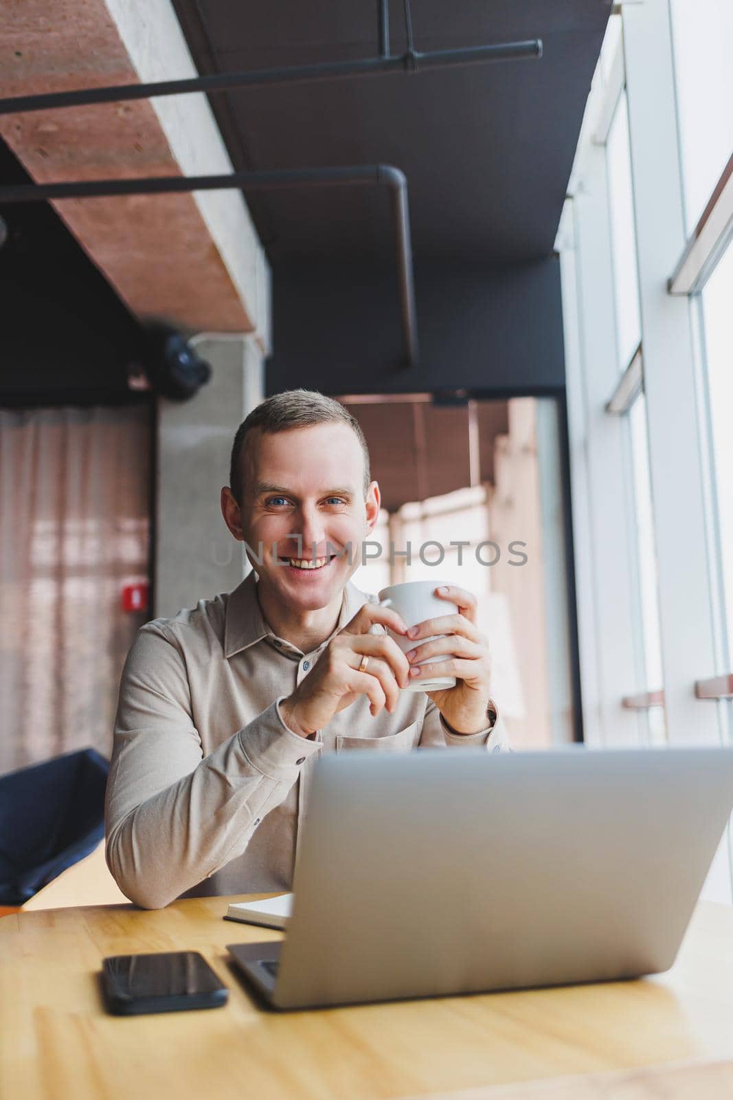 A young smart man is sitting in the office with a cup of coffee and is working on a project related to public cyber technology. Businessmen with laptop trying to meet deadlines in external marketing.