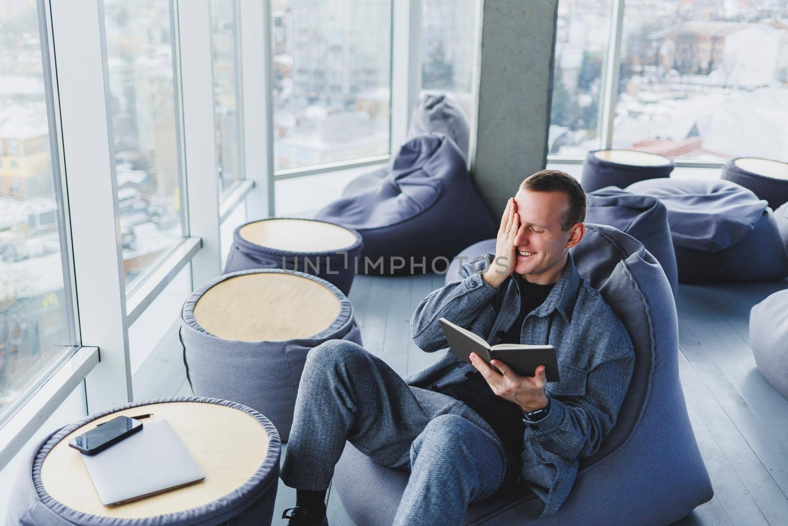 A male businessman in a casual suit resting in a comfortable pouf while working, an attractive freelancer in a suit works remotely and checks notes in a notebook by Dmitrytph