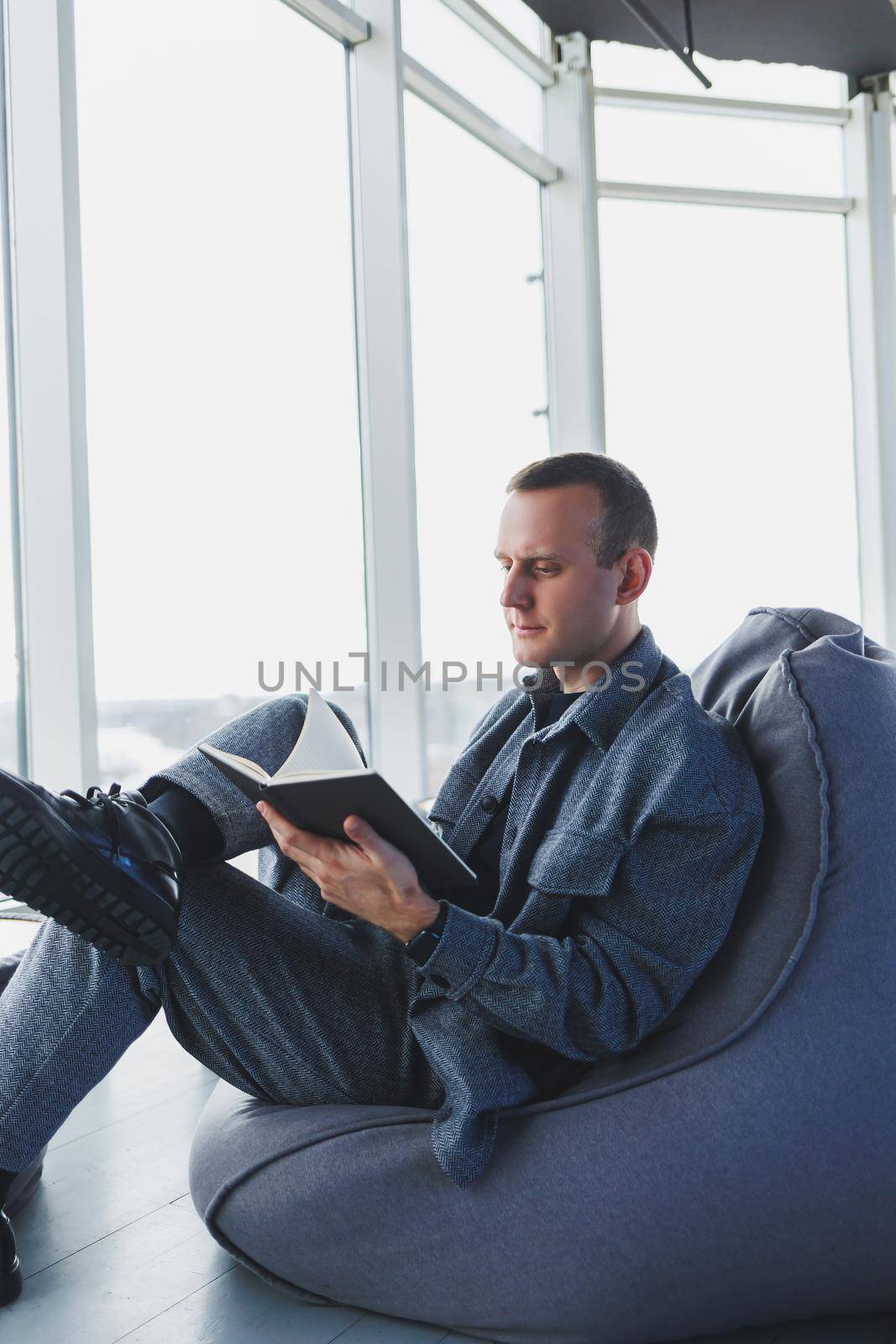 A male businessman in a casual suit resting in a comfortable pouf while working, an attractive freelancer in a suit works remotely and checks notes in a notebook