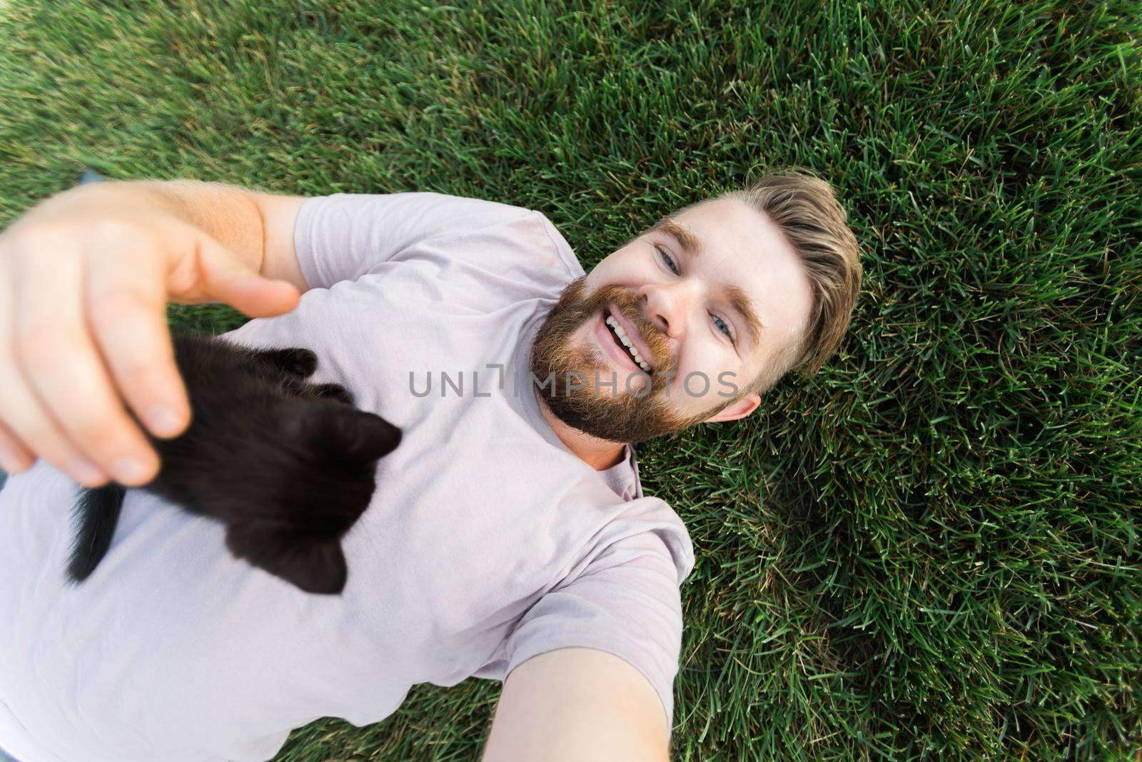 Man with little kitten lying and playing on grass - friendship love animals and pet owner concept by Satura86