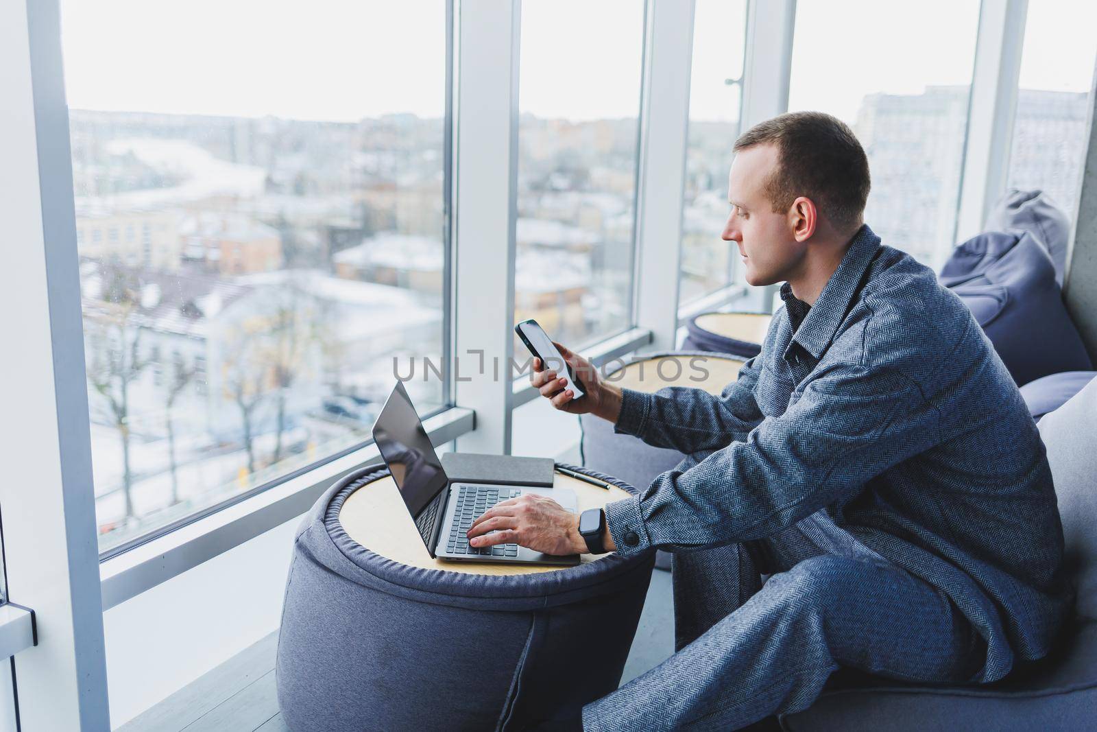 Break. Smiling young man relaxing on bean bag chair while sitting at table and relaxing using laptop, happy businessman leaning back, enjoying work, feeling satisfied