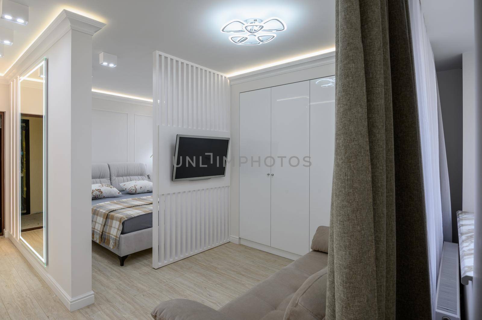 Studio flat interior with living room and bedroom, television and a closet in it's corner with a mirror