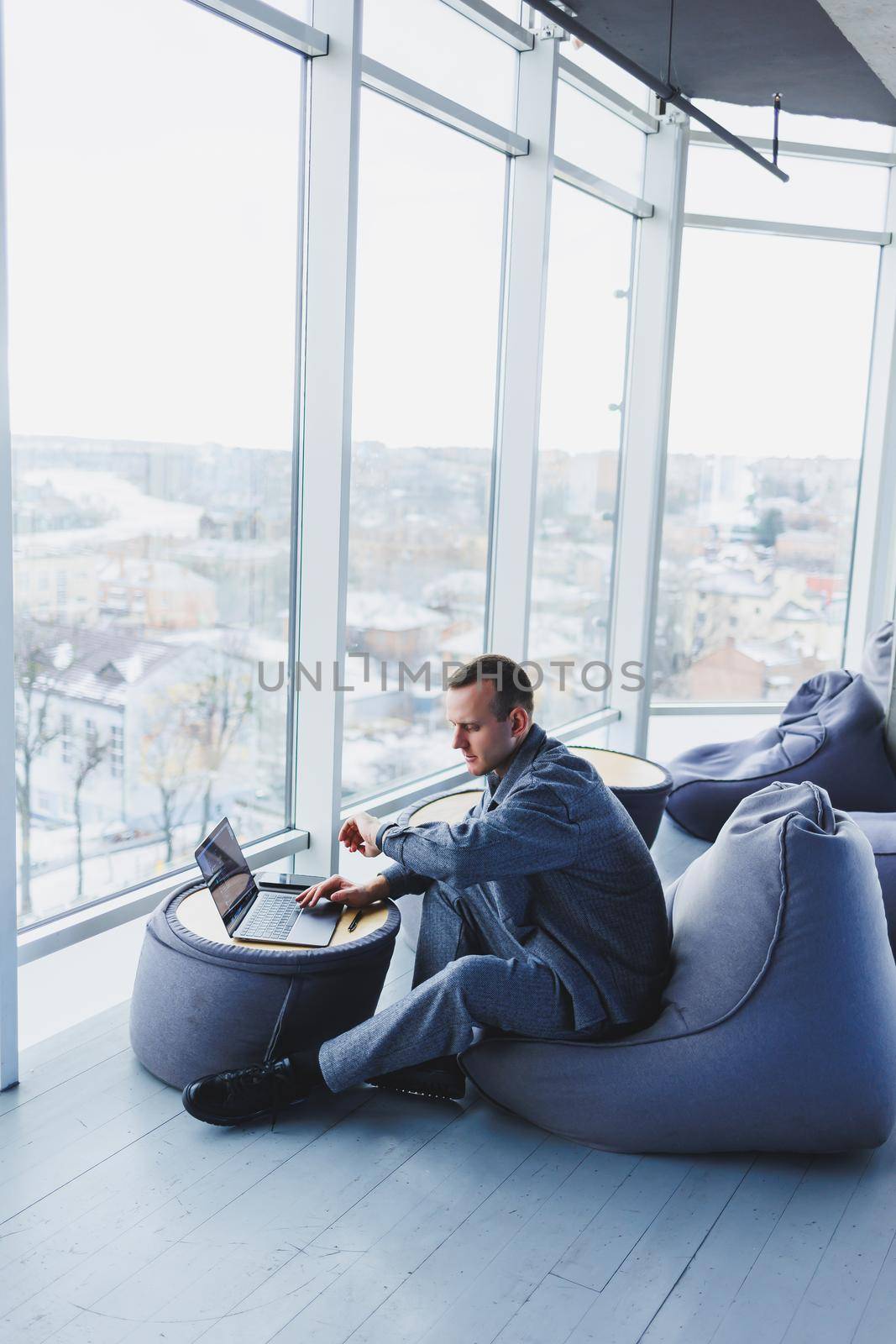 Break. Smiling young man relaxing on bean bag chair while sitting at table and relaxing using laptop, happy businessman leaning back, enjoying work, feeling satisfied