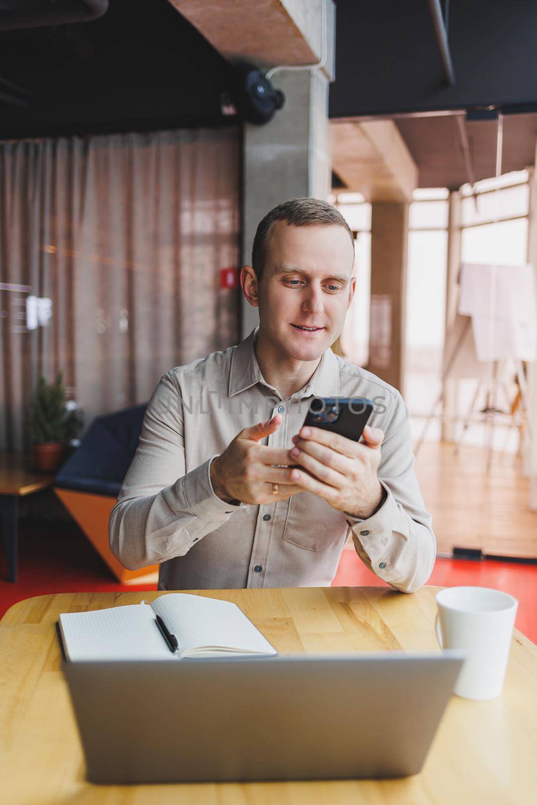A young smart man is sitting in the office with a cup of coffee and is working on a project related to public cyber technology. Businessmen with laptop trying to meet deadlines in external marketing.