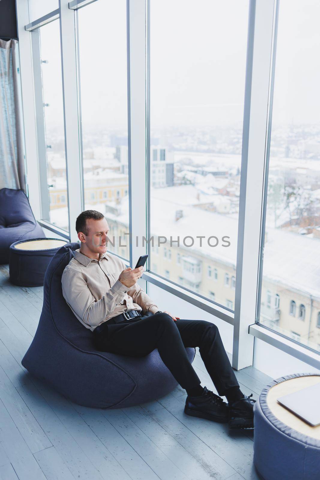 Successful male freelancer sitting in modern workspace and checking notifications on mobile phone in casual clothes. Remote work.