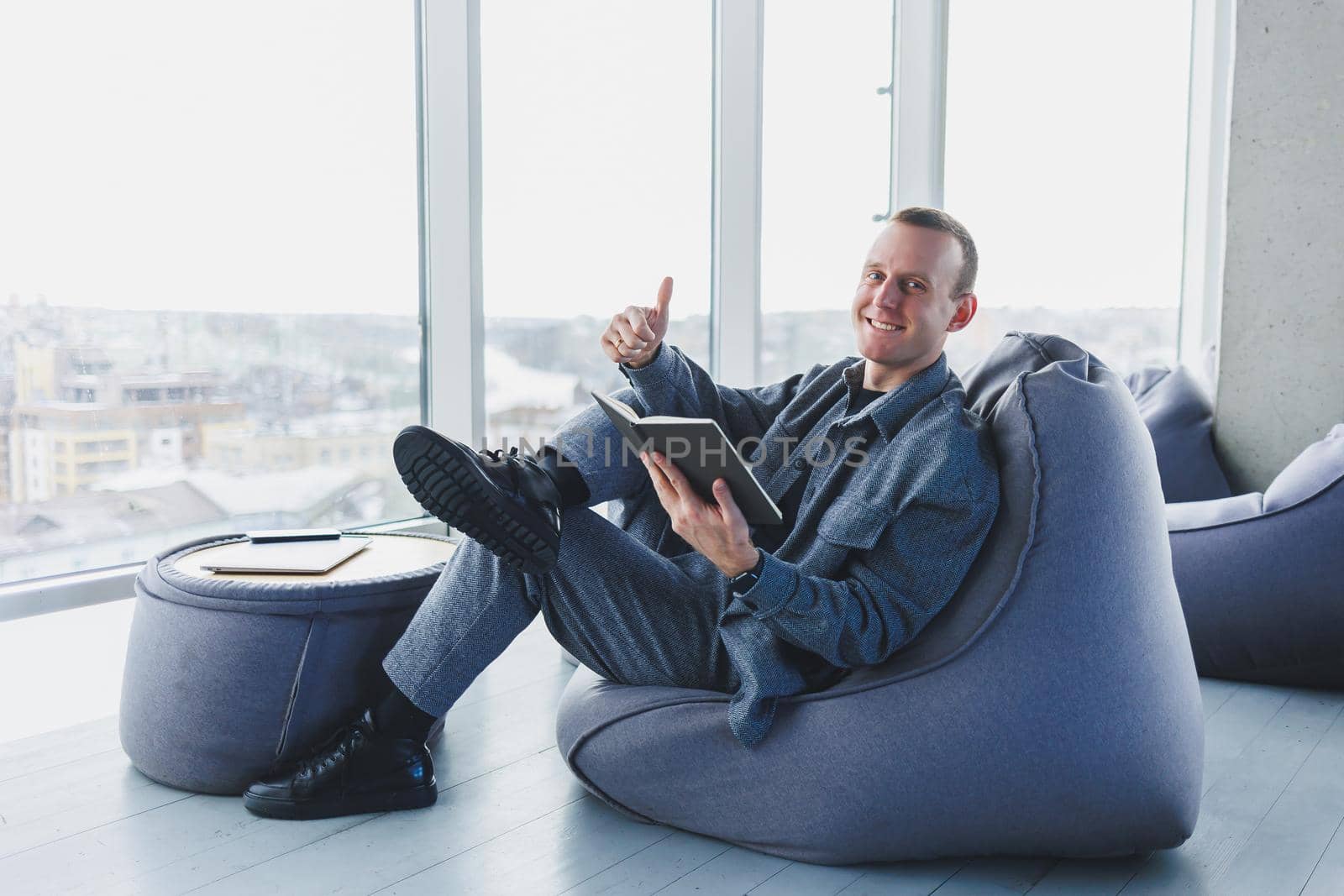 A male businessman in a casual suit resting in a comfortable pouf while working, an attractive freelancer in a suit works remotely and checks notes in a notebook