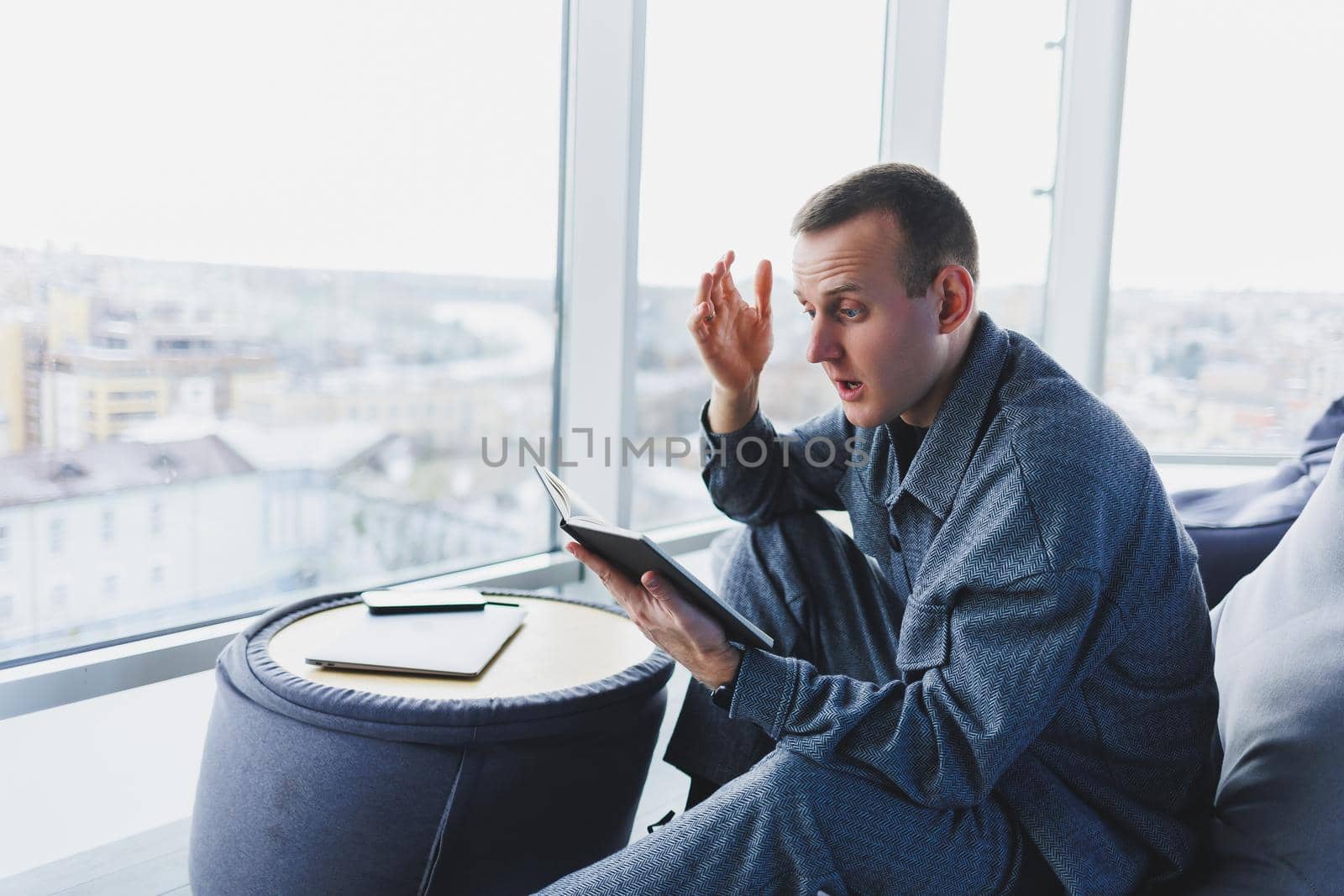 A male businessman in a casual suit resting in a comfortable pouf while working, an attractive freelancer in a suit works remotely and checks notes in a notebook