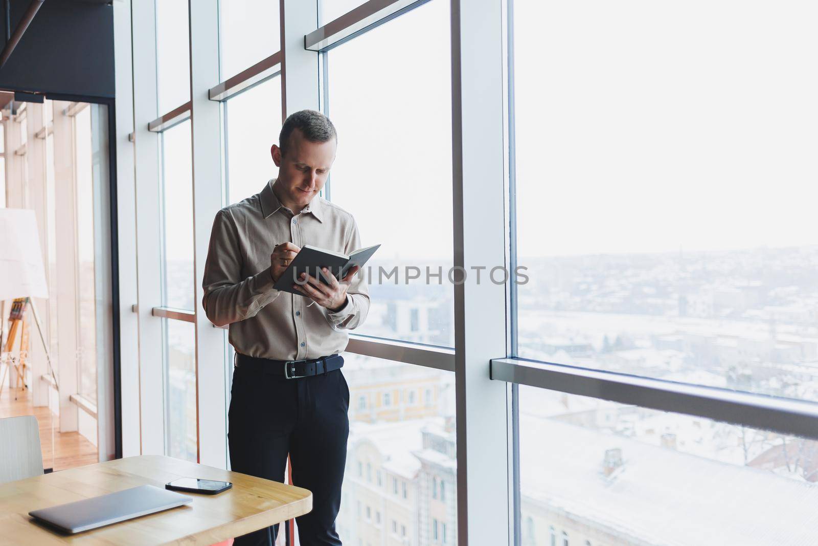 Intelligent young male using laptop to take notes during online education program, experienced male freelancer sitting with technology in cafe interior. Young businessman